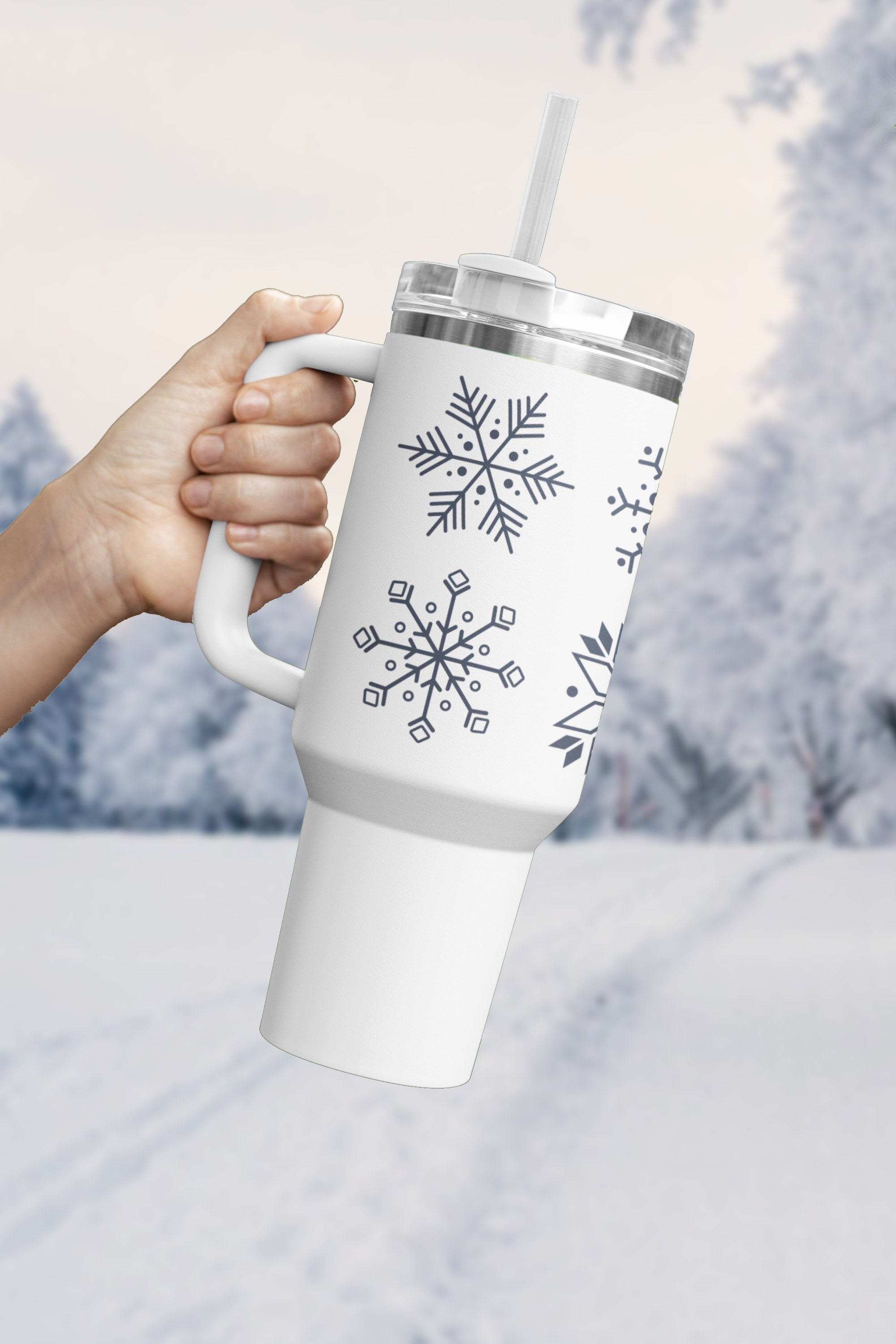 Person holding a stainless steel tumbler with blue snowflake design, BPA-free and insulated, against a snowy outdoor background.